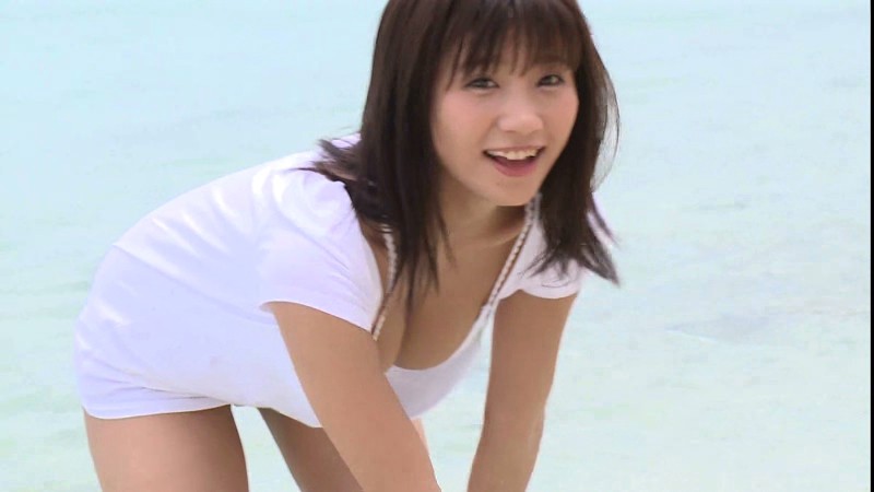 白いTシャツ姿で浜辺ではしゃぐ葉月あや。爽やかな笑顔が印象的なワンシーン。